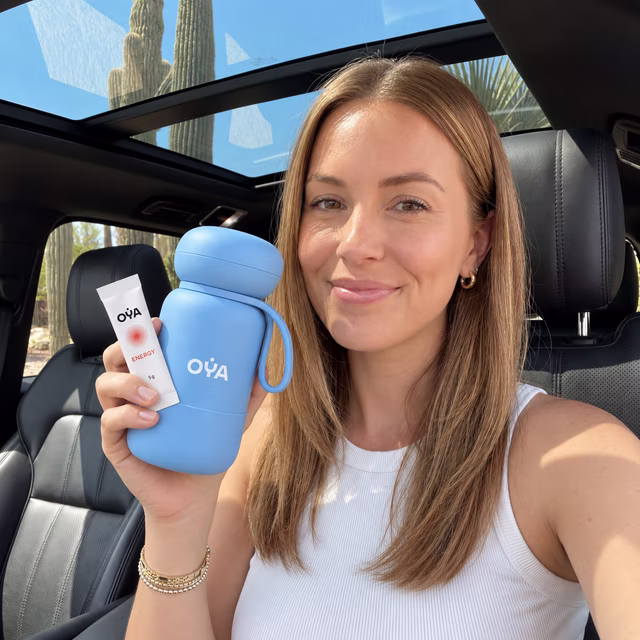 Une femme en voiture, la gourde OYA et un stick à la main